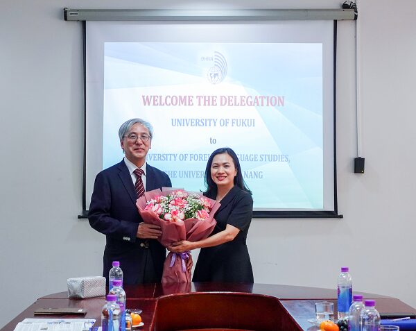 A person and person holding flowers in front of a projector screenDescription automatically generated